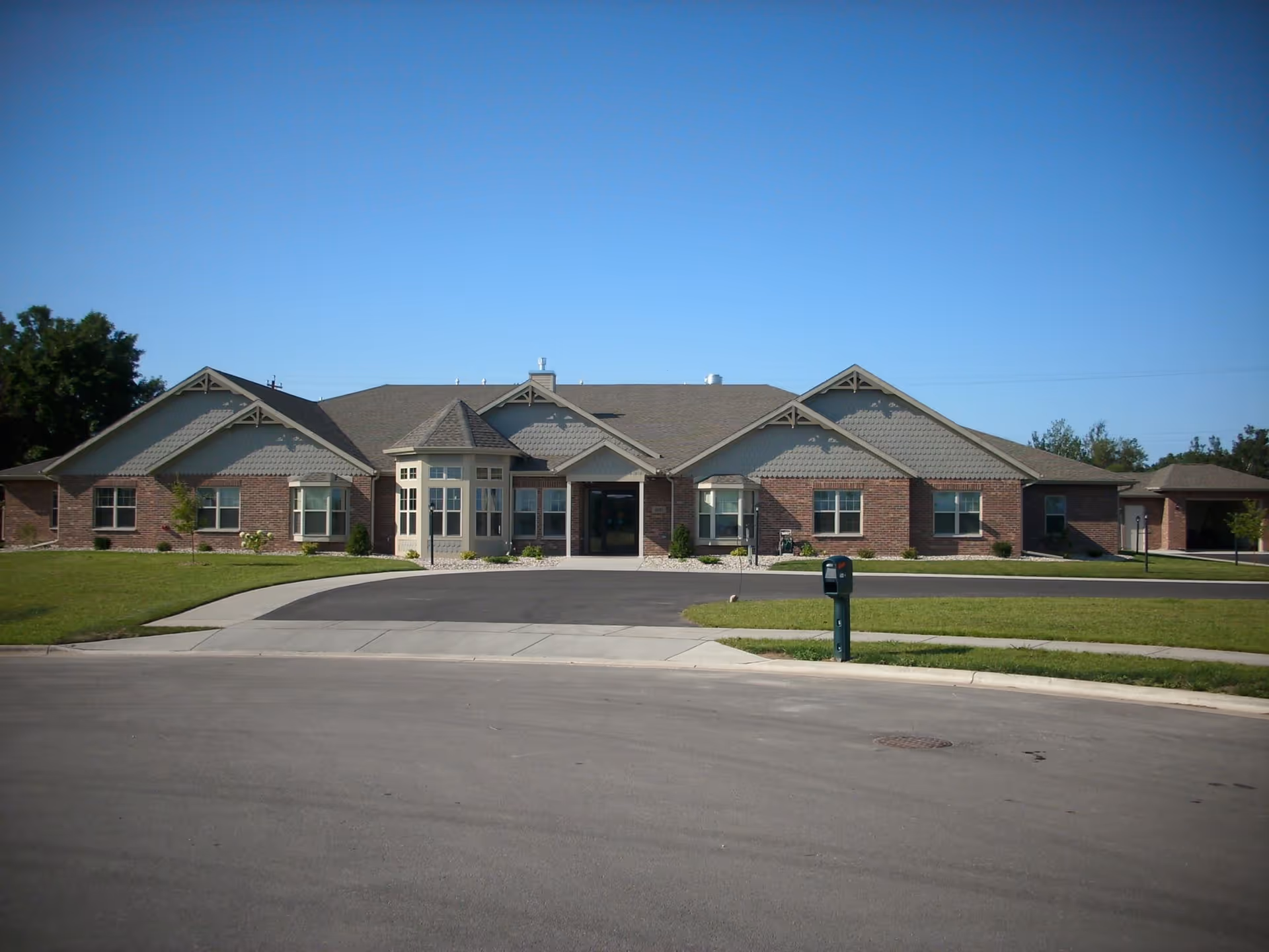 Single-story brick senior living facility with manicured lawn and driveway.