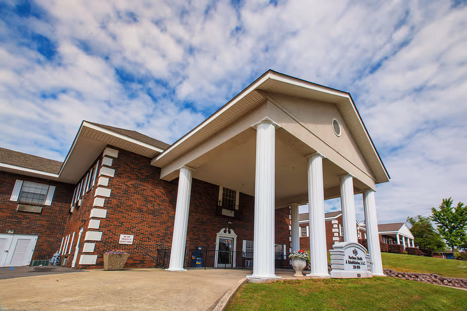 Exterior view of Northway Health and Rehabilitation, LLC building with large white columns supporting a covered entrance, red brick walls, and a partly cloudy sky above.