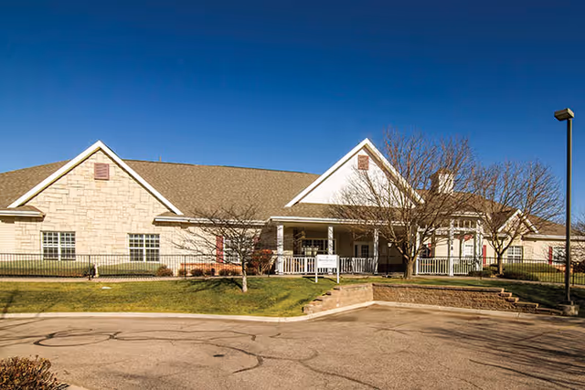 Front view of a single-story building with a covered porch, stone facade, landscaped lawn and clear blue sky.