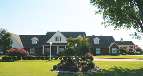 Front view of a single-story brick assisted living building with a manicured lawn and landscaped shrubs.