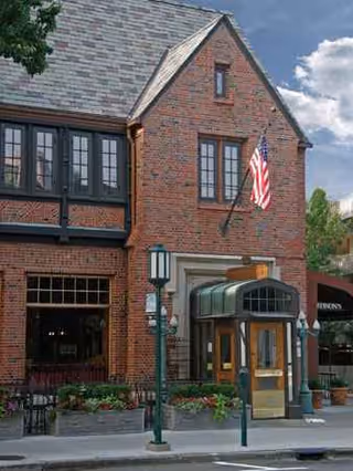 Brick Baldwin House exterior with American flag, glass entrance, and sidewalk.