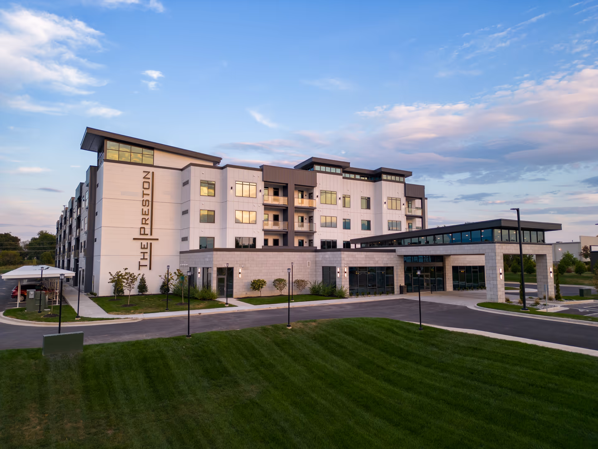 Front view of a modern multi-story senior living building named 'The Preston' with a landscaped lawn and covered entrance.