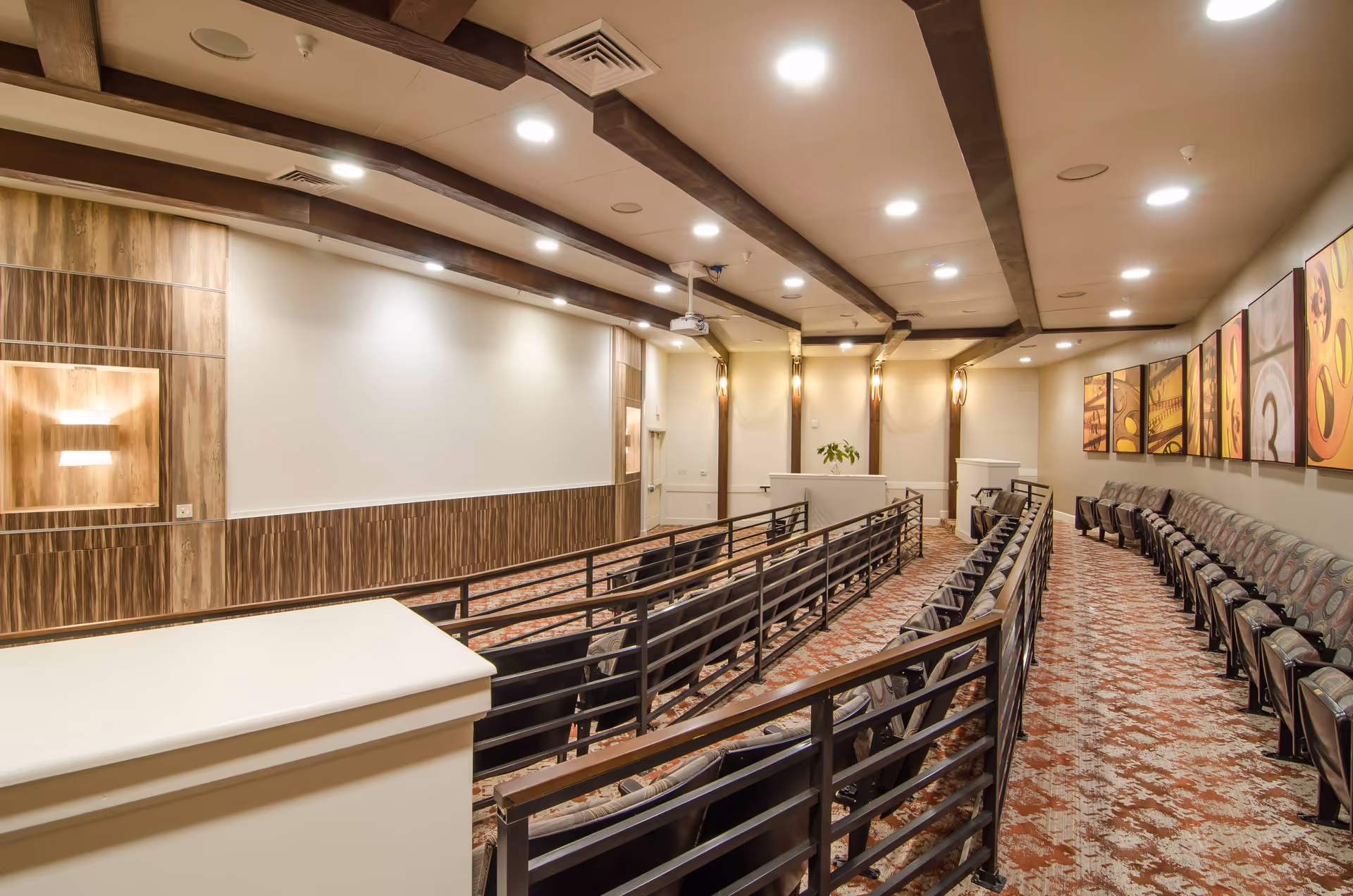 Interior view of a small screening/auditorium room with tiered rows of chairs facing a large projection screen and ceiling-mounted projector.