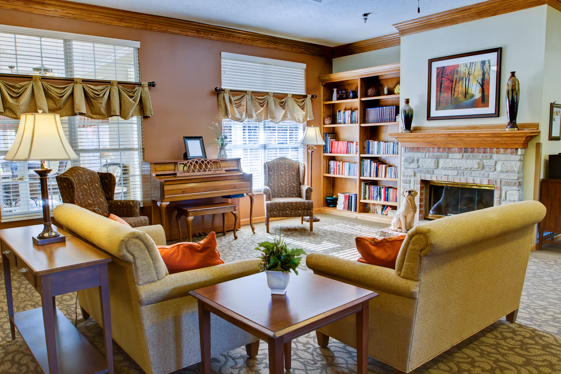 A cozy living room with two sofas and a coffee table facing armchairs, a piano, a bookshelf, and a fireplace.