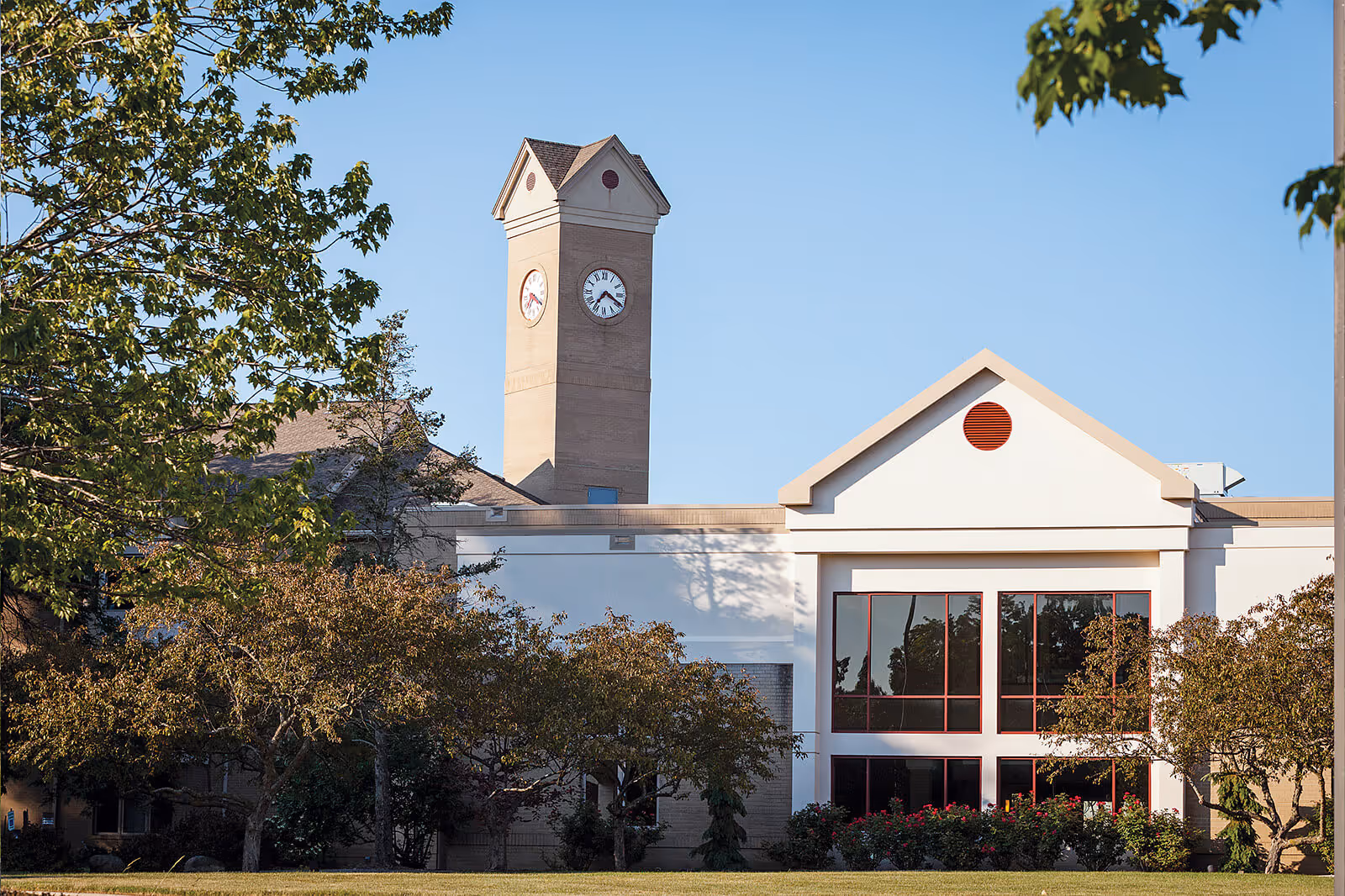Exterior view of a building with a clock tower, surrounded by trees and bushes under a clear blue sky.