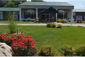 Front exterior view of Williamsport Nursing and Rehabilitation building with a green lawn, red flowers, shrubs, and a covered entrance.