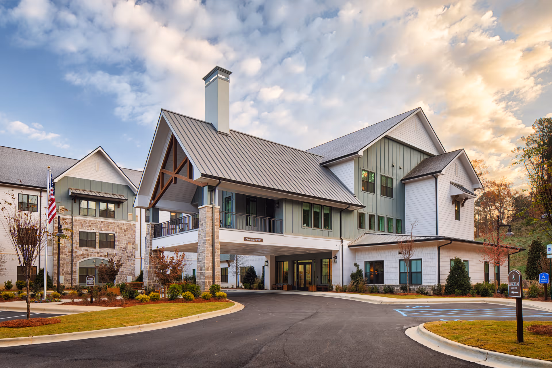 Front entrance of a modern senior living facility with a covered porte-cochère, landscaped driveway, and an American flag.