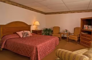 A furnished bedroom in a senior living facility with a bed, chairs, and dresser.