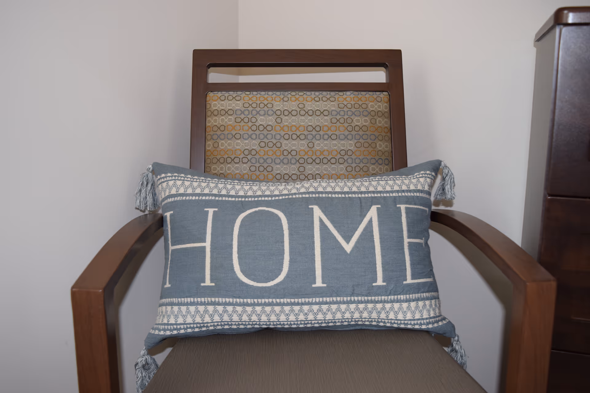 Wooden armchair with a patterned backrest and a blue decorative pillow that reads "HOME".