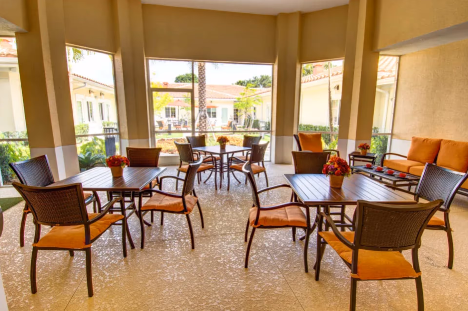 Covered outdoor patio with brown wicker chairs around tables and floral centerpieces.