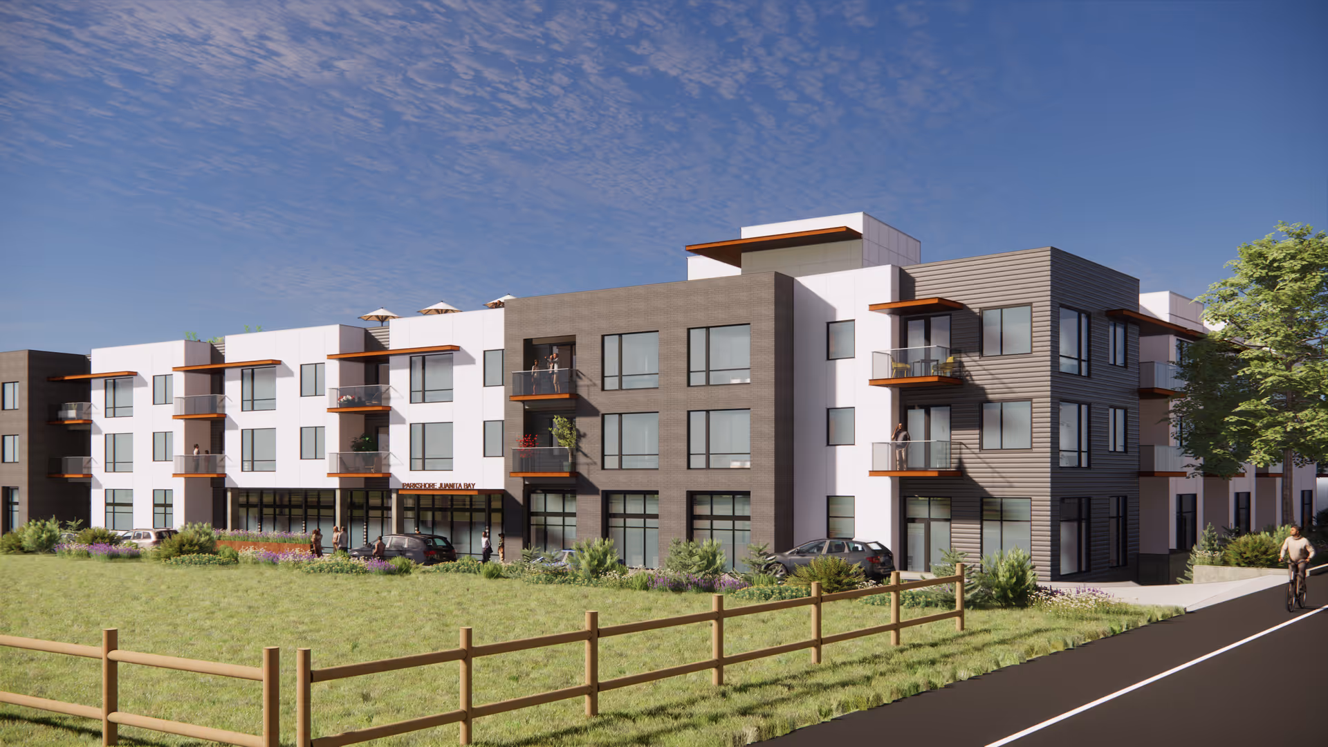 Three-story modern residential building with balconies, large windows, landscaping and a fenced grassy front lawn under a blue sky.