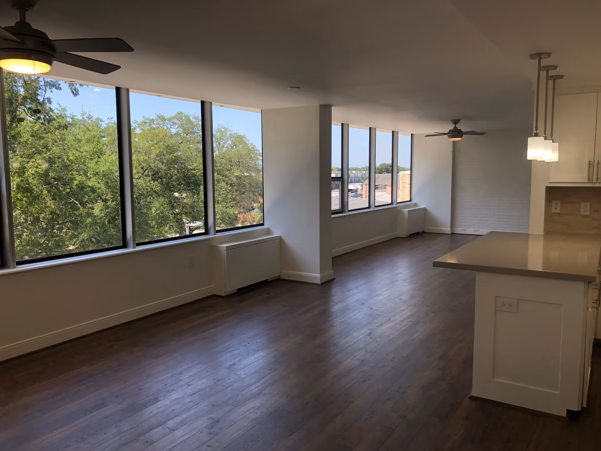 Spacious open-plan living area with large windows, hardwood floors, ceiling fans, and a kitchen island.