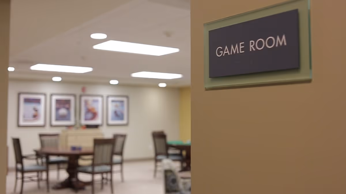 View into a game room with tables and chairs and a wall sign reading "GAME ROOM".