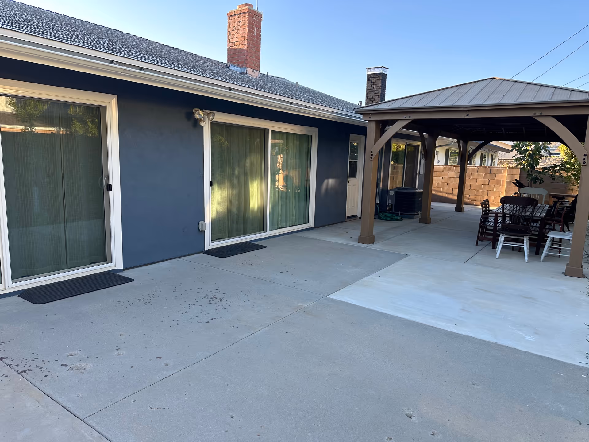 Blue building exterior with sliding glass doors and a covered outdoor patio area with tables and chairs.