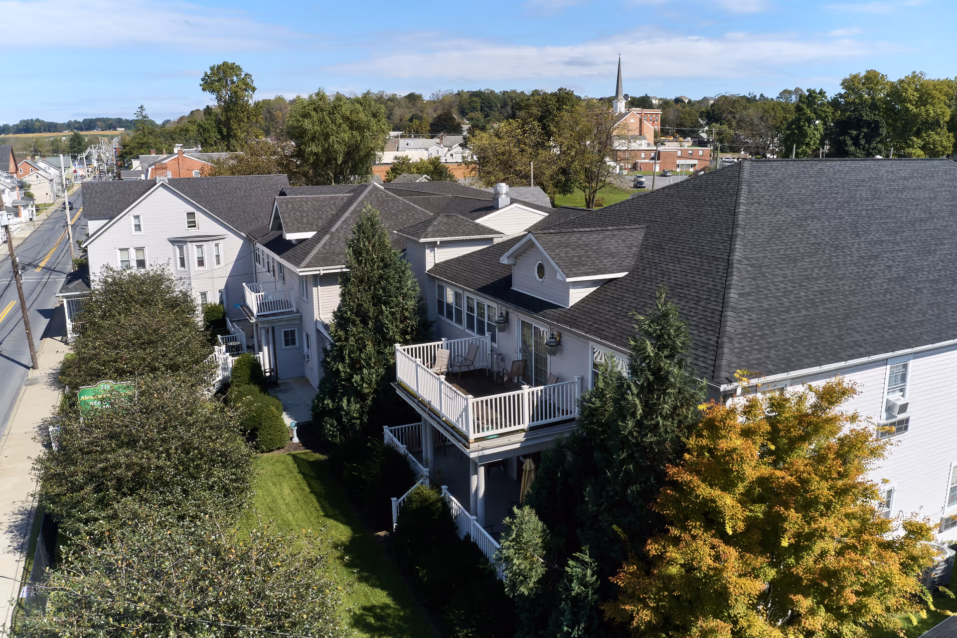 Aerial view of Alexandria Manor of Bath showing multi-story senior living buildings with balconies, landscaped lawns, trees, and the nearby town.