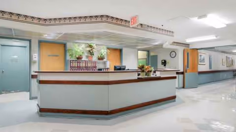 Bright hospital-like reception area with a curved desk, plants, and pastel walls.