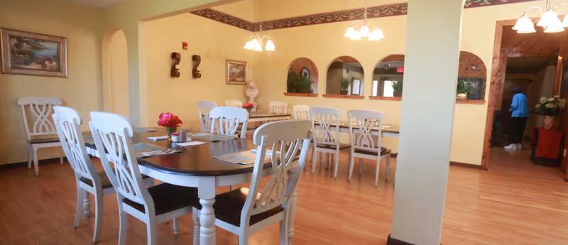 Dining room with several dark-top tables and white chairs on hardwood floors under pendant lights and decorative arches.