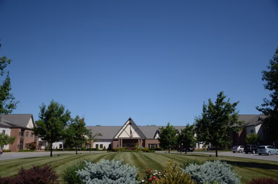 Front exterior view of Preswick Glen facility with a well-maintained lawn, trees, shrubs, and a clear blue sky.
