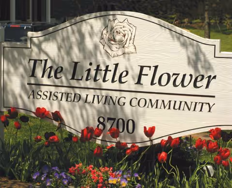 Exterior sign for The Little Flower Assisted Living Community with red tulips in front