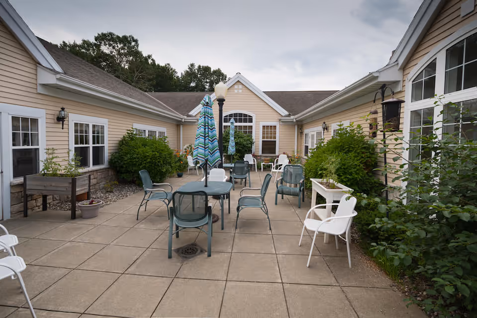 Outdoor courtyard patio with tables, chairs and umbrellas between single-story beige senior living buildings