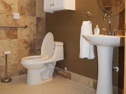 Accessible bathroom with toilet, pedestal sink, grab bar, and tiled walls.