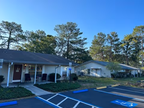 Front view of single-story senior living cottages with covered porches, landscaping, and accessible parking spaces.