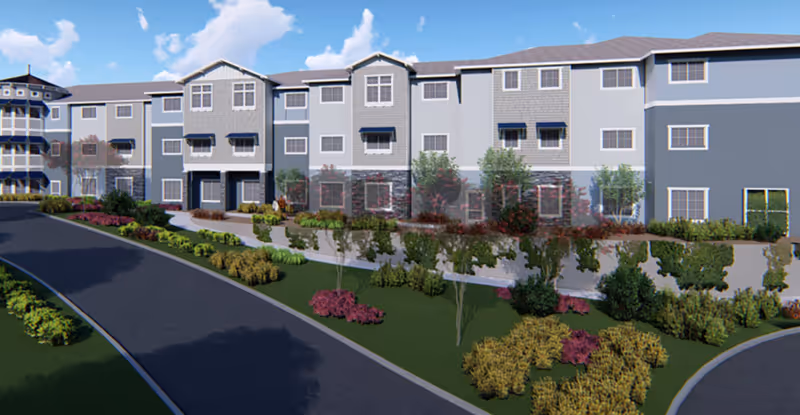 Front exterior of a three-story senior living building with a curved driveway and landscaped shrubbery.
