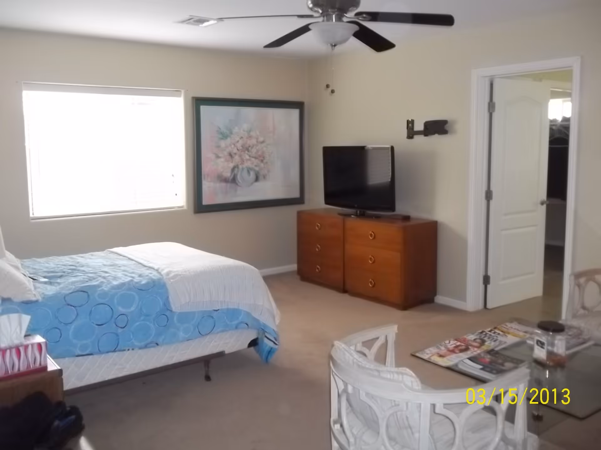 Neat bedroom with a bed, ceiling fan, dresser with a TV, window, wall art, and a small table with chairs.