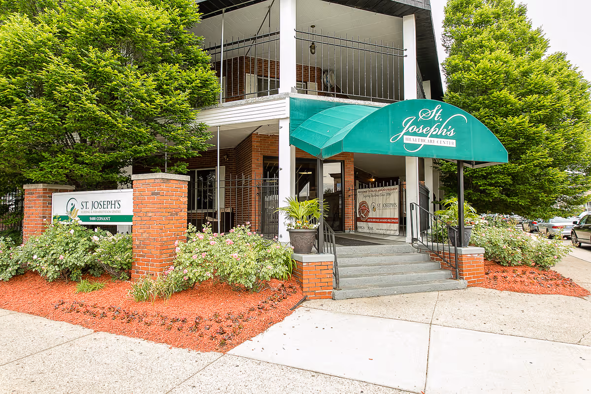 Front entrance of St. Joseph's healthcare center with a green awning, brick pillars, steps and landscaped flower beds.