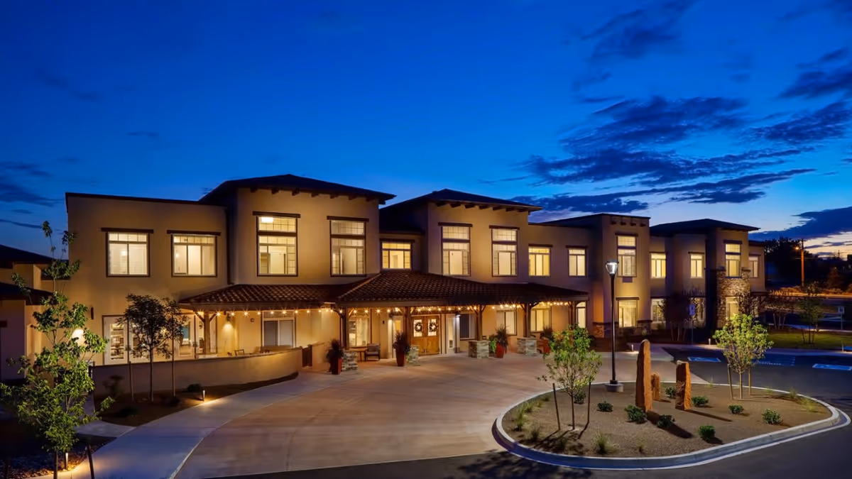 Dusk view of the illuminated two-story MorningStar Assisted Living & Memory Care building with a covered drive-up entrance and landscaped circular driveway.