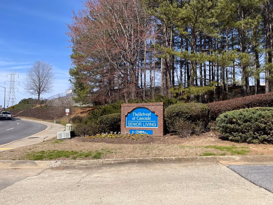 Brick entrance sign reading 'The Retreat at Cascade Senior Living' set among shrubs and trees beside a road.