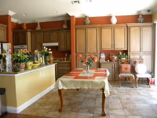 Cozy kitchen-dining area with wooden cabinets, tiled floor, and a central table with flowers.