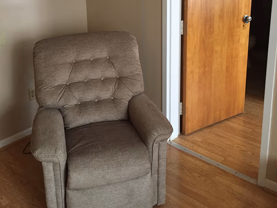 Beige upholstered recliner on wood floors beside an open wooden door.