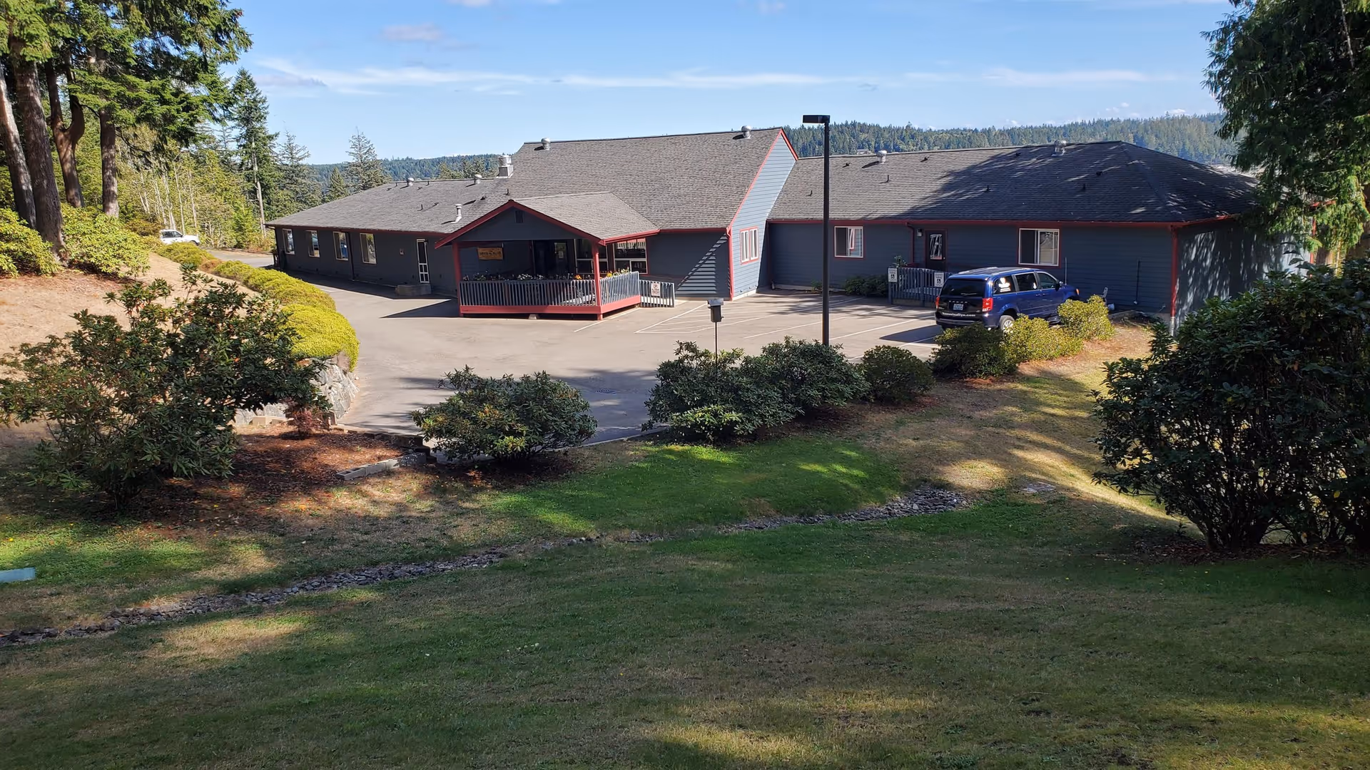 Single-story assisted living building with a covered entrance and parked car, surrounded by landscaped lawns and trees.