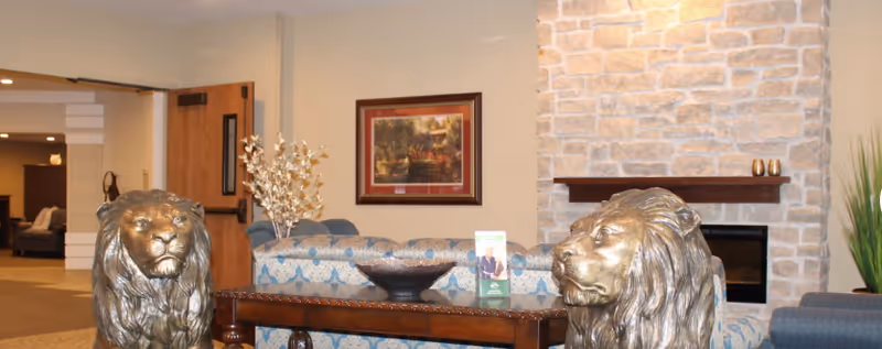 Lobby lounge with two bronze lion statues flanking a wooden table in front of upholstered seating and a stone fireplace.