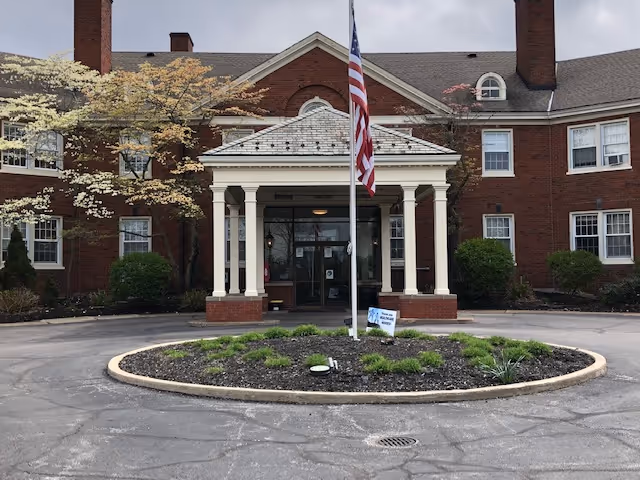 Brick building entrance with flagpole, circular driveway, and landscaped island in front.
