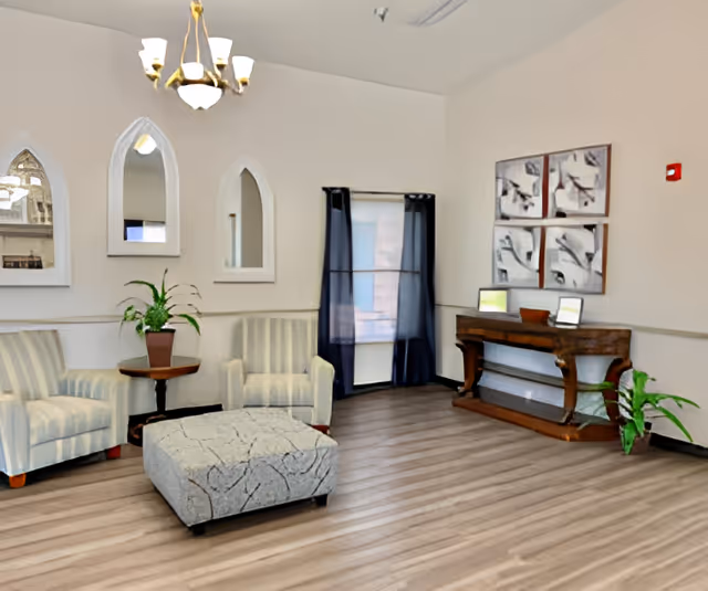 A bright lounge with striped armchairs, a patterned ottoman, a wooden console table, plants and wall decor.