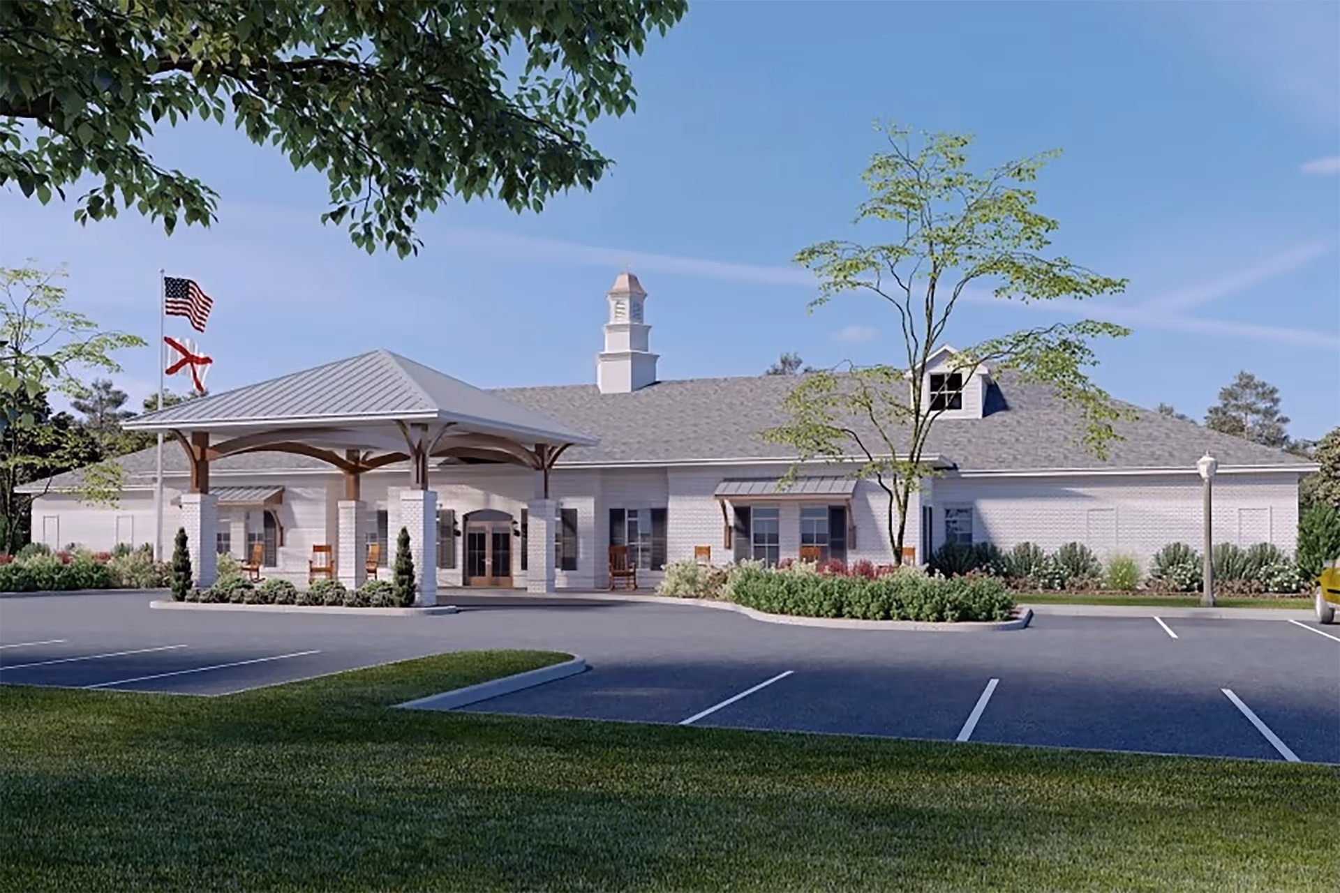 Exterior view of Carillon Oaks Mobile facility showing a single-story building with a covered entrance, landscaped greenery, American and Alabama state flags, and a parking lot in the foreground under a clear blue sky.