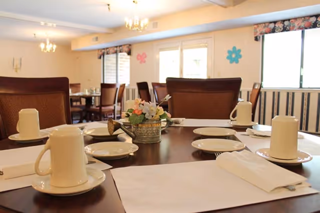 A dining room table set with cups, saucers, napkins and a floral centerpiece in a senior living facility dining area.