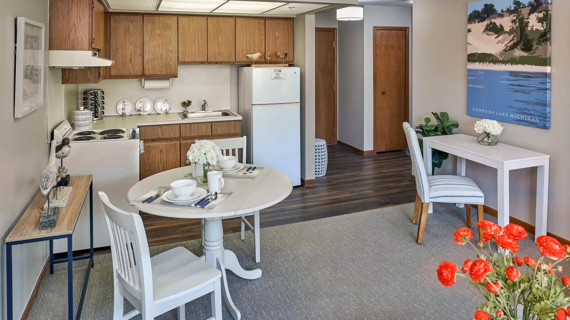 Open studio-style interior with a kitchenette, a round dining table set for two, chairs, and a small desk.