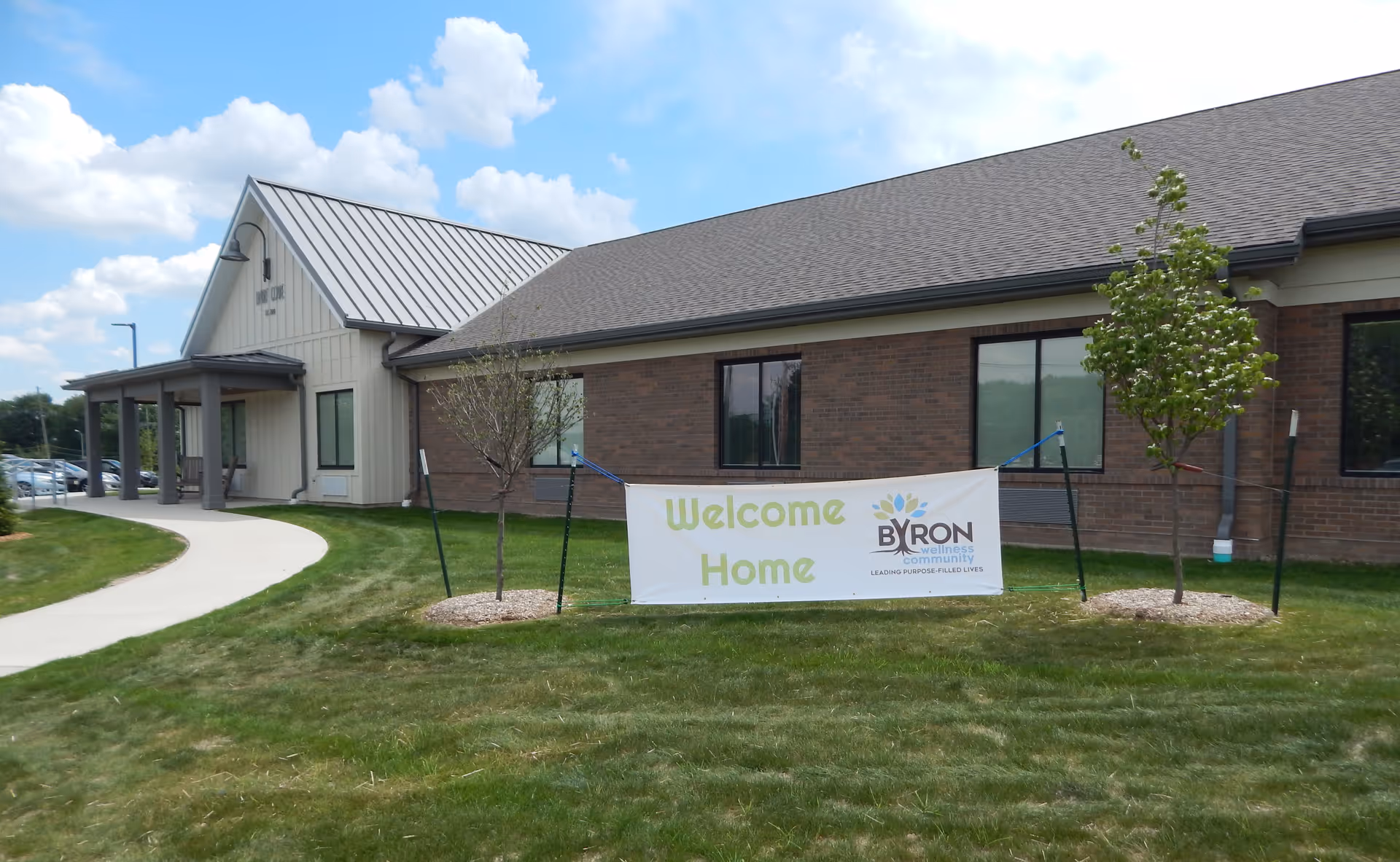 Front exterior of Byron Health Center with a 'Welcome Home' banner on the lawn in front of the entrance.
