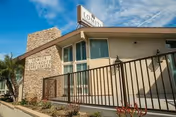 Exterior view of Lomita Post-Acute Care Center building with a stone facade, beige walls, a black metal fence, and a clear blue sky with some clouds.