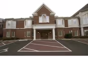 Brick two-story building front with a covered entrance portico and marked parking area.