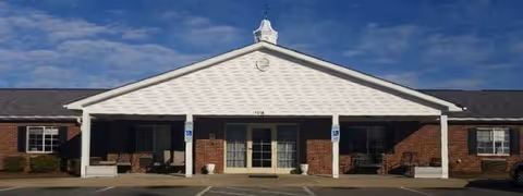 Facade of The Canterbury House senior living facility with white portico and benches.