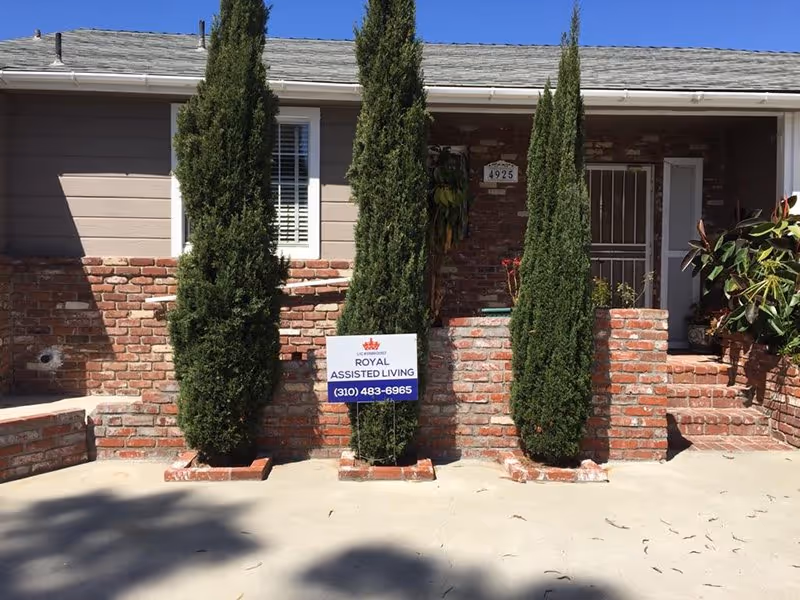 Brick front entrance with three tall trees and a Royal Assisted Living sign.