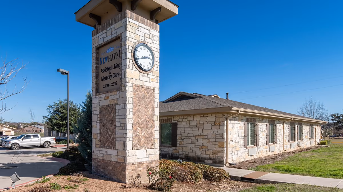 Stone clock-tower sign marks New Haven Assisted Living building in a sunny lot.