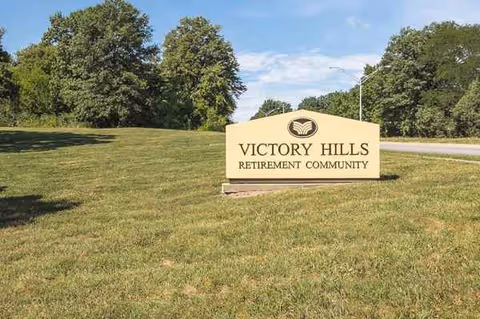 Exterior view of Victory Hills Retirement Community sign on a grassy lawn with trees