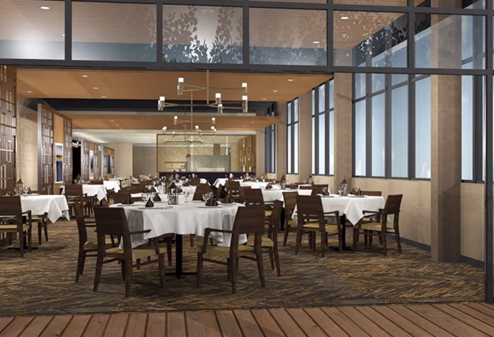 Spacious dining room with round tables covered in white tablecloths and wooden chairs under modern lighting fixtures.