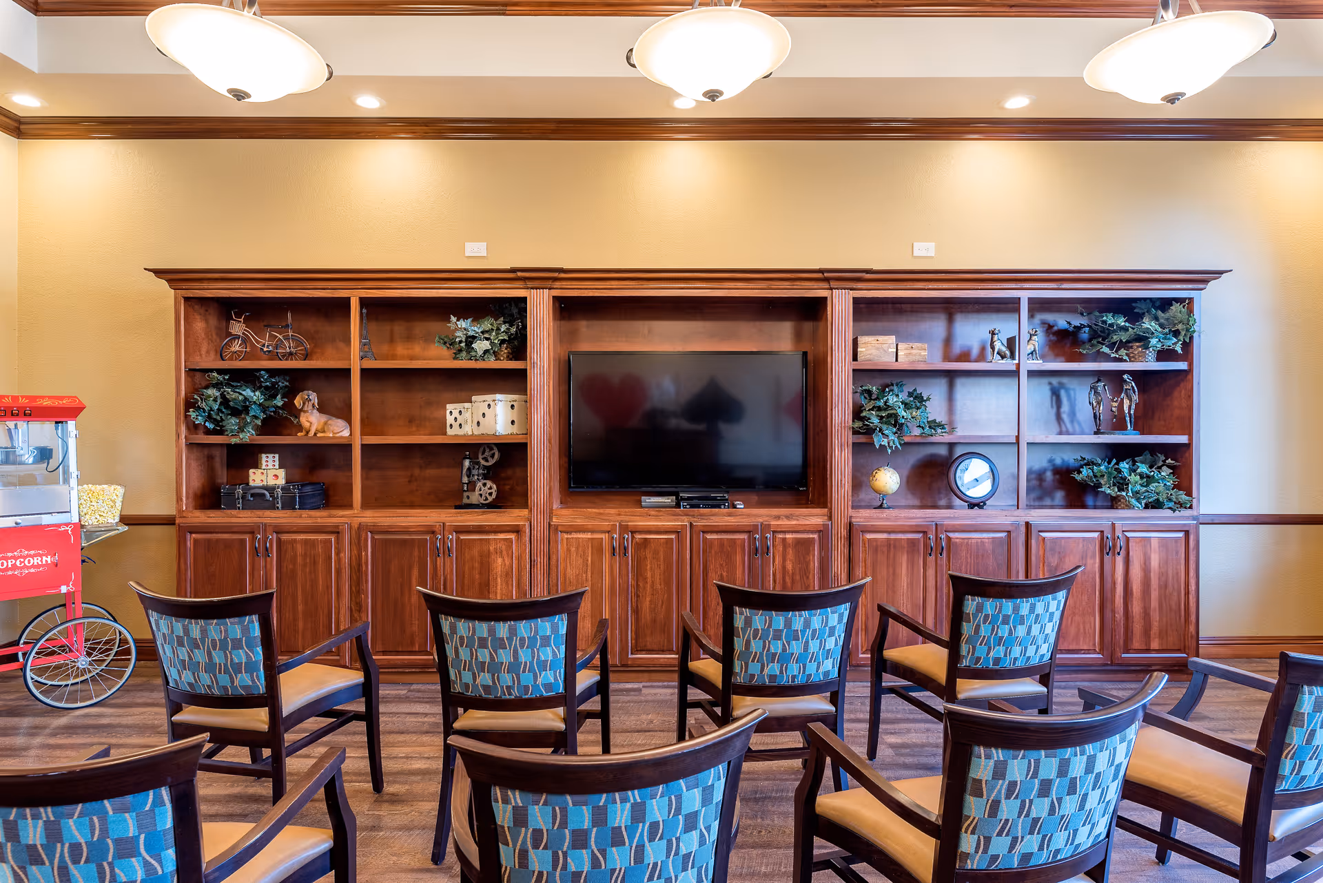Rows of chairs facing a large wooden built-in shelving unit with a TV and decorative items in a common room.