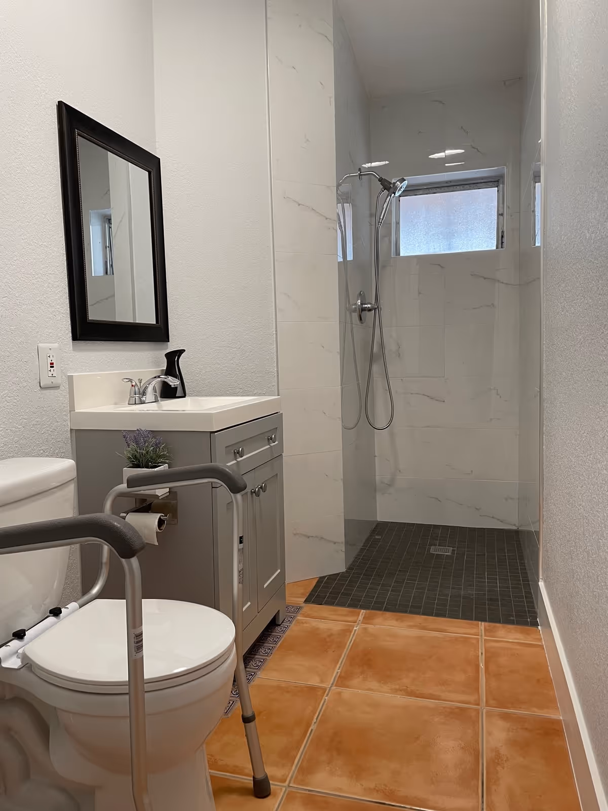 Accessible bathroom with a toilet and safety rails, a vanity with mirror, and a walk-in tiled shower.